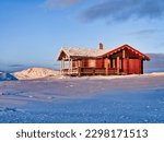 A red Norwegen timber house in a frozen landscape during a winter sunrise in Eidfjord, Norway