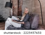 Gorgeous blonde fashion model relaxing at home, sitting with book on cozy chair looks aside happily  against modern interior. Successful businesswoman relaxing after hard week. Purposeful female.