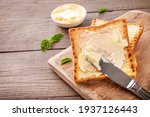 Knife spreading butter on toast bread on wooden background. Copy space.