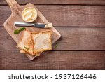 Slices of toast bread with butter on cutting board on wooden background. Top view. Copy space.