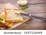 Knife spreading butter on toast bread on wooden background.