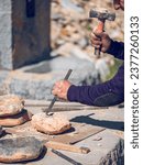 Small photo of Crop anonymous craftsman cutting rock using chisel and hammer while creating stone craft on workbench in sunny day
