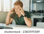 Anxious male employee sitting at table and touching forehead while speaking on phone in modern workspace