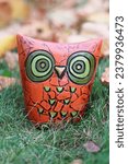 Small photo of Vintage thrifted retro kitsch 1970s-style orange owl piggy bank with green eyes displayed in the grass during fall.