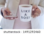 Professional woman using mobile phone and holding a cup that says LIKE A BOSS