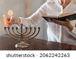 Small photo of Woman lighting first candle of Chanukah on Menorah with the shamash