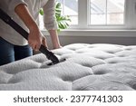 Woman using vacuum cleaner to vacuum mattress in a bedroom