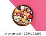 Chocolate candies, top view plate of chocolate candies. Wrapped multicolored foil. Almond candies. Isolated white and pink background. Copy space. Traditional Turkish feast called bayram sweets.