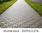 A sidewalk made of rectangular artificial stone extending into the distance in yellow and gray with a green lawn, texture backgrounds for graphic design. Abstract wallpaper.