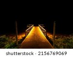 A beautiful shot of a wooden pier illuminated by light at night