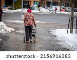 An elderly woman walking with the help of a walker in a snowy winter