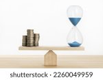 Small photo of Time and money balance concept Sand clock and stacked coins on Seesaw Copy space