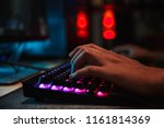 Hands of professional gamer boy playing video games on computer in dark room using backlit colorful keyboard