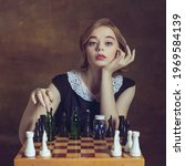 Small photo of Ready for game. Young woman in art action isolated on brown background. Retro style, comparison of eras concept. Beautiful female model like legendary chess player, queen or duchess, old-fashioned.