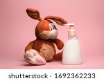 Small photo of funny and cute rabbit slob dirty looks at a bottle of soap shampoo or cream soap the importance of hygiene and hand washing for children, disinfection. Pink background