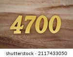 Small photo of Wooden Arabic numerals 4700 painted in gold on a dark brown and white patterned plank background.