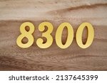 Small photo of Wooden numerals 8300 painted in gold on a dark brown and white patterned plank background.