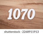 Small photo of White number 1070 on a brown and light brown wooden background.