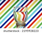 Small photo of Optical illusion created by refracting light with a glass of water and colored diagonal lines