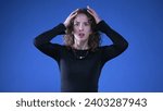 Small photo of Anxious apprehensive woman reacting with shock and despair to news by putting arms on top of head and covering mouth in disbelief and surprise