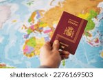 Small photo of Hand Holding The Spanish Passport Over The World Pap. Business Travel, Identification, Security And Boarding Concept