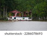 View of white riverboat and house on stilts on the Amazon riverbank, depicting lifestyle at Amazonas riverbank