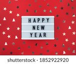 Happy New Year greeting on light box and confetti on a red background.