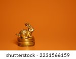 A metal rabbit figurine with coins on a bright background. Financial symbol. The year of the rabbit.