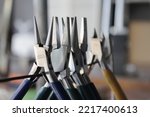 Round nose pliers, flat pliers and other jewelry making tools for cutting and bending wire at the jewellers bench in a professional jewellery workshop. Steel equipment with colorful handles.