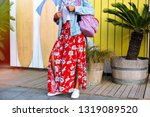 Fashion details of stylish woman posing near beach cafe, USF boards and palms trees, wearing hipster outfit, maxi floral feminine skirt, denim jacket and backpack, summer spring travel vibes.