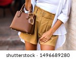 Street style fashion details, tanned woman wearing linen shorts, white shirt, brown leather bag and clear beige sunglasses, modern classic summer chic outfit, warm colors.