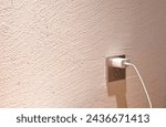 Small photo of white mobile phone charger stabbing in plug in socket on room wall