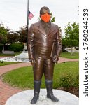 Small photo of Edwardsville, Illinois/USA - May 11, 2020 : Statue of Ninean Edwards wearing an orange crochet face mask during the COVID-19 pandemic with American flag at half-mast in background