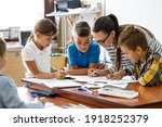 Small photo of Female teacher helps school kids to finish they lesson.They sitting all together at one desk.