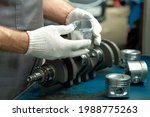 Small photo of Spare parts.The piston of an automobile engine is in the hands of an auto mechanic. Side view. On the desktop is a set of pistons and a crankshaft. Close-up, side view.Car engine repair