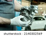 Small photo of Repair and maintenance in the car center. An auto mechanic holds a turbine in his hands. Inspection and control of spare parts. Checking the conformity and integrity of the turbine before installing i