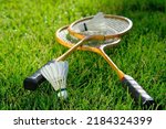 A set of badminton rackets and two feather shuttlecocks lie on a green grass lawn for outdoor play.