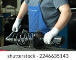 Small photo of Repair and maintenance of the car at the dealership. An auto mechanic replaces the spring and shock absorber strut of the front suspension of the car.