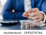 Small photo of Businessman holding euro cents coins dollar bills on table with pile of coins and banks calculator, managing dividing money to save and invest it to make income. Saving money and investing concept.