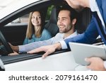 Small photo of Car test-drive concept. Caucasian young family testing trying new car before buying purchasing it while male shop assistant helping them to choose with digital tablet.