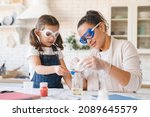 Scientific experiment at home. Laboratory tests for school homework. Parent mother with daughter kid making chemical test at home kitchen. Nanny babysitter teacher help in protective glasses
