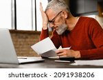 Small photo of Expensive charges on domestic bills. Loan, debt, bunkruptcy concept. Closeup sad depressed caucasian businessman holding documents, having problems with dismissal at home office