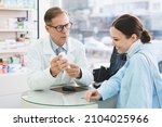 Small photo of Drugstore pharmacy consultation. Caucasian male pharmacist druggist advising selling medicines, pills, drugs, painkillers, vitamins to a female customer client, buyer in drugstore