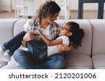 Small photo of Childcare and nurturing. African mother holding little preteen girl daughter, spending time together and having fun. Nanny childminder playing with kid child at home
