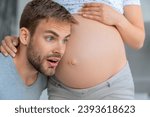 Small photo of Handsome man is listening to his beautiful pregnant wife's tummy and excited. Future father feeling hearing first bumps of baby embryo fetus. Parenting