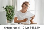 Small photo of Caucasian young woman working remotely, reading official letter, financial report, billing overdue, documents at home office. Freelancer doing paperwork