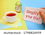 Small photo of Cup of tea and a notebook with the inscription Simplify your life. Conceptual photo Office of your day job. Take the easy way.