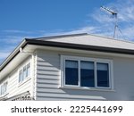 Residential detached house with white wooden plank walls and metal roof. Eaves and gutter with downspout.