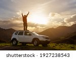person with arms raised and on the roof of his off-road car watching the sunset on the mountain after a day of travel and adventure. Active turism. mountain activities.