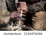 Bushcraft man making feather stick with knife to start fire
